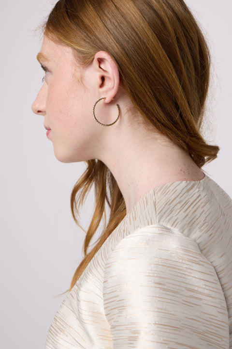 Close-up of a person wearing a gold hoop earring against a plain background