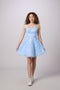 A young woman modeling a light blue sleeveless A-line dress with a textured floral lace bodice and a flared tulle skirt, paired with white sneakers, against a solid light gray studio background.
