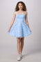 A young woman modeling a light blue sleeveless A-line dress with a textured floral lace bodice and a flared tulle skirt, paired with white sneakers, against a solid light gray studio background.