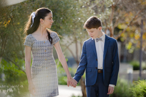 Two children, a girl in a dress and a boy in a suit, holding hands outdoors.