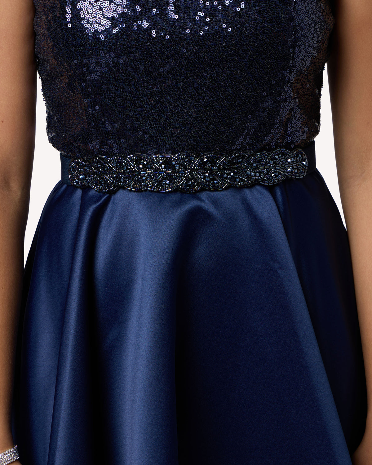 Close-up of a navy blue formal dress with a sequined lace bodice, a beaded waistband, and a satin skirt.