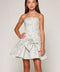 A young girl modeling a strapless light blue and white floral-patterned dress with a large bow at the waist, set against a plain light gray studio background.