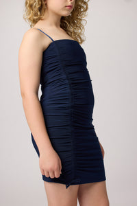 Blonde wearing an Un Deux Trois fitted ruched dress in navy blue with nude heel.