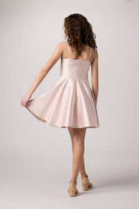 Brunette girl in an Un Deux Trois light pink jacquard fit and flare dress.