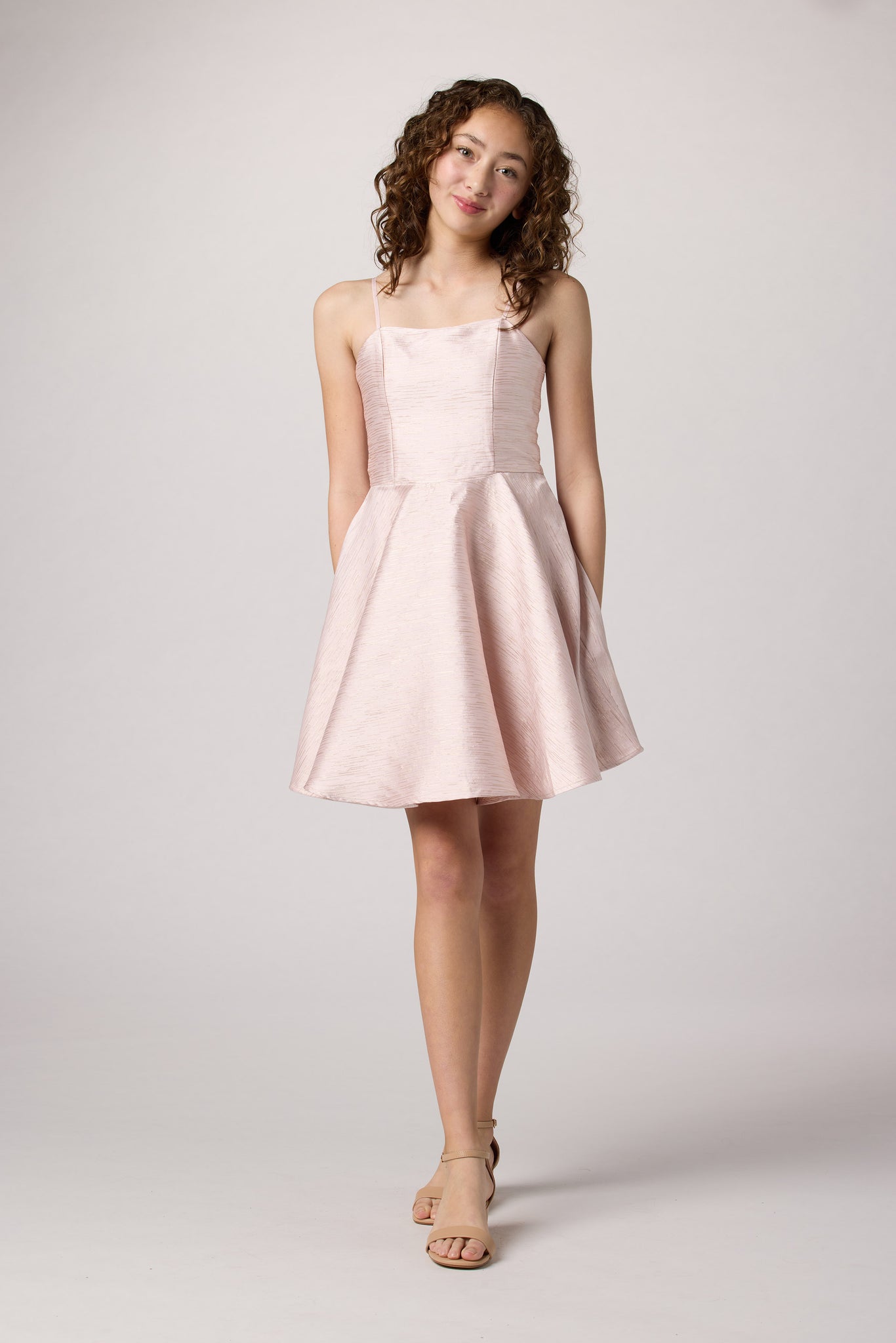 Brunette girl in an Un Deux Trois light pink jacquard fit and flare dress.