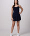A young woman modeling a navy blue sleeveless mini dress with a tiered skirt, paired with white sneakers, against a light gray studio background.