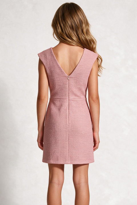 A child model shown from the back wearing a dusty pink sleeveless dress with a deep V-neckline and a central zipper, set against a textured light gray background.