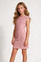 A young girl with long wavy blonde hair wearing a textured dusty pink sleeveless fit-and-flare dress, standing against a light gray textured studio background.