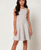A sleeveless fit-and-flare dress with a small white grid pattern on a light beige background, modeled by a young woman against a plain light gray studio backdrop.