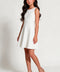 A young girl with long dark hair models a sleeveless white textured mini dress with a flared skirt, paired with beige ankle-strap block-heel sandals, against a plain light gray studio background.