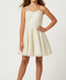 A young girl modeling a short, sleeveless cream dress with thin spaghetti straps, a sweetheart neckline, and a flared skirt, paired with nude high-heeled sandals against a light gray studio background.