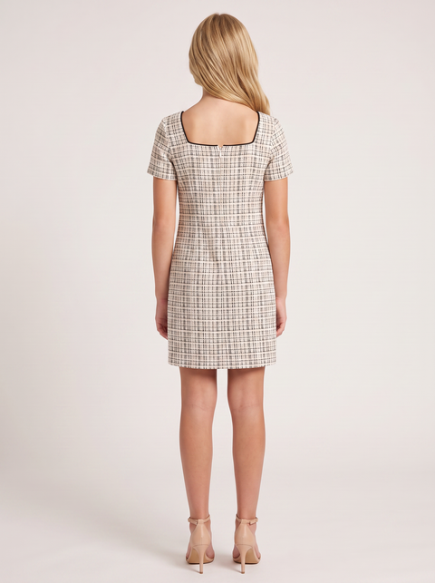 A woman viewed from the back wearing a short-sleeve square-neck dress with a beige and black windowpane plaid pattern, paired with nude high heels, set against a plain light beige studio background.