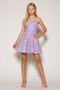 A young girl with long blonde hair models a strapless lavender and white patterned mini dress with a flared skirt, paired with beige high-heeled sandals, against a plain light gray studio background.
