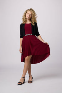 Blonde girl in a pleated high low burgundy dress with black shoe and bolero.