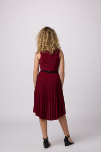 Blonde girl in a pleated high low burgundy dress with black shoe.