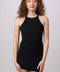 A woman with curly brown hair wearing a black ribbed halter-neck mini dress, standing against a solid light gray studio background.