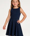 A young girl with light brown hair wearing a sleeveless navy blue skater dress, standing against a plain white studio background.