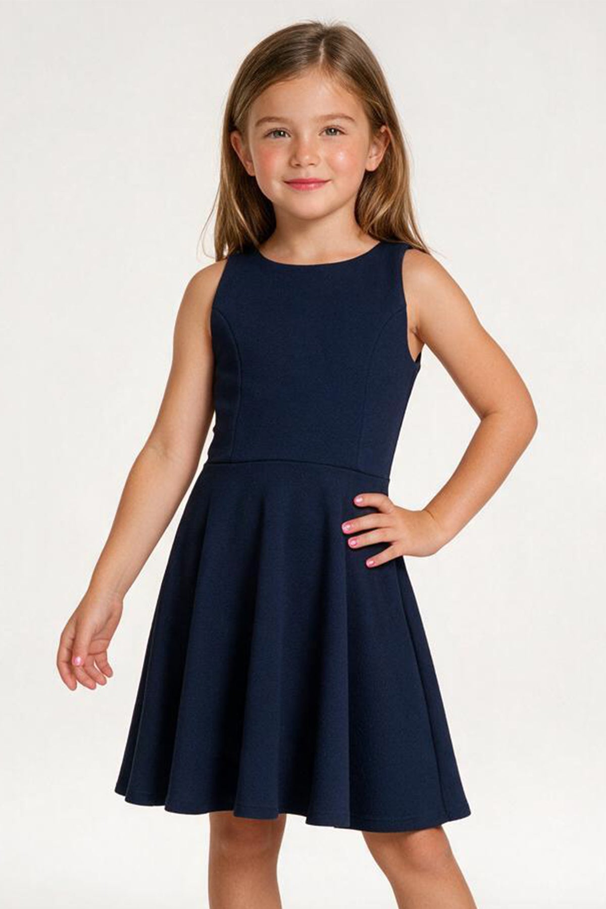 A young girl with light brown hair wearing a sleeveless navy blue skater dress, standing against a plain white studio background.