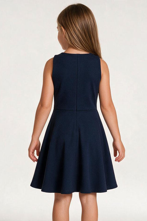 A young girl viewed from the back wearing a sleeveless navy blue fit-and-flare dress against a plain light background.