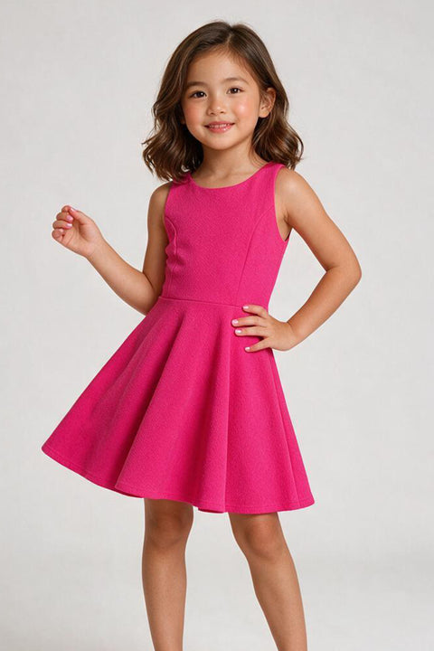 A young girl with shoulder-length brown hair models a sleeveless bright pink A-line dress against a light gray studio background.