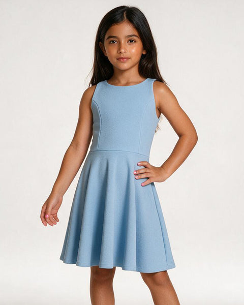 A young girl with long dark hair wearing a sleeveless light blue A-line dress, standing against a plain off-white studio background.
