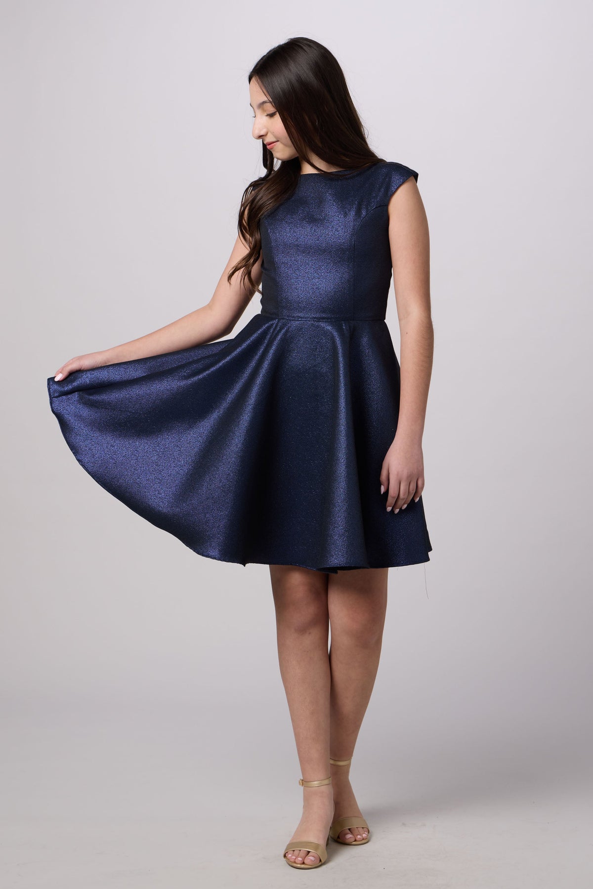 A woman modeling a sleeveless, knee-length navy blue dress with a flared skirt, posed against a light gray studio background.