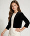 A young girl with long brown hair models a black velvet cropped jacket over a cream-colored dress against a light gray studio background.