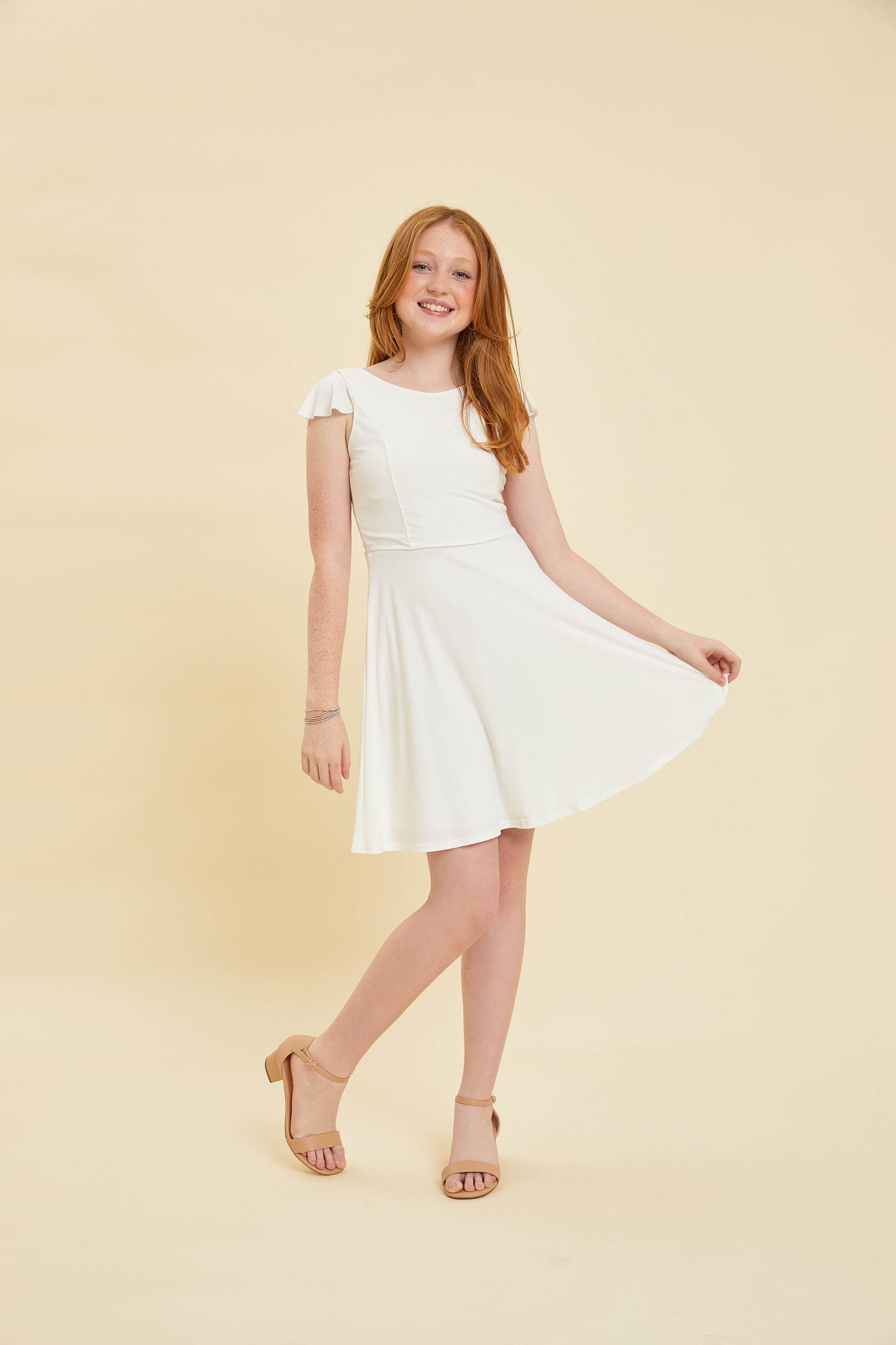 Red head in an ivory flutter sleeve dress and nude heel.