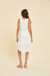 Brunette in ivory pleated high low dress with belt and nude shoe.