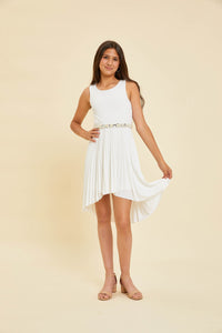 Brunette in ivory pleated high low dress with belt and nude shoe.