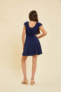 Brunette wearing a navy flutter sleeve dress with nude shoes.
