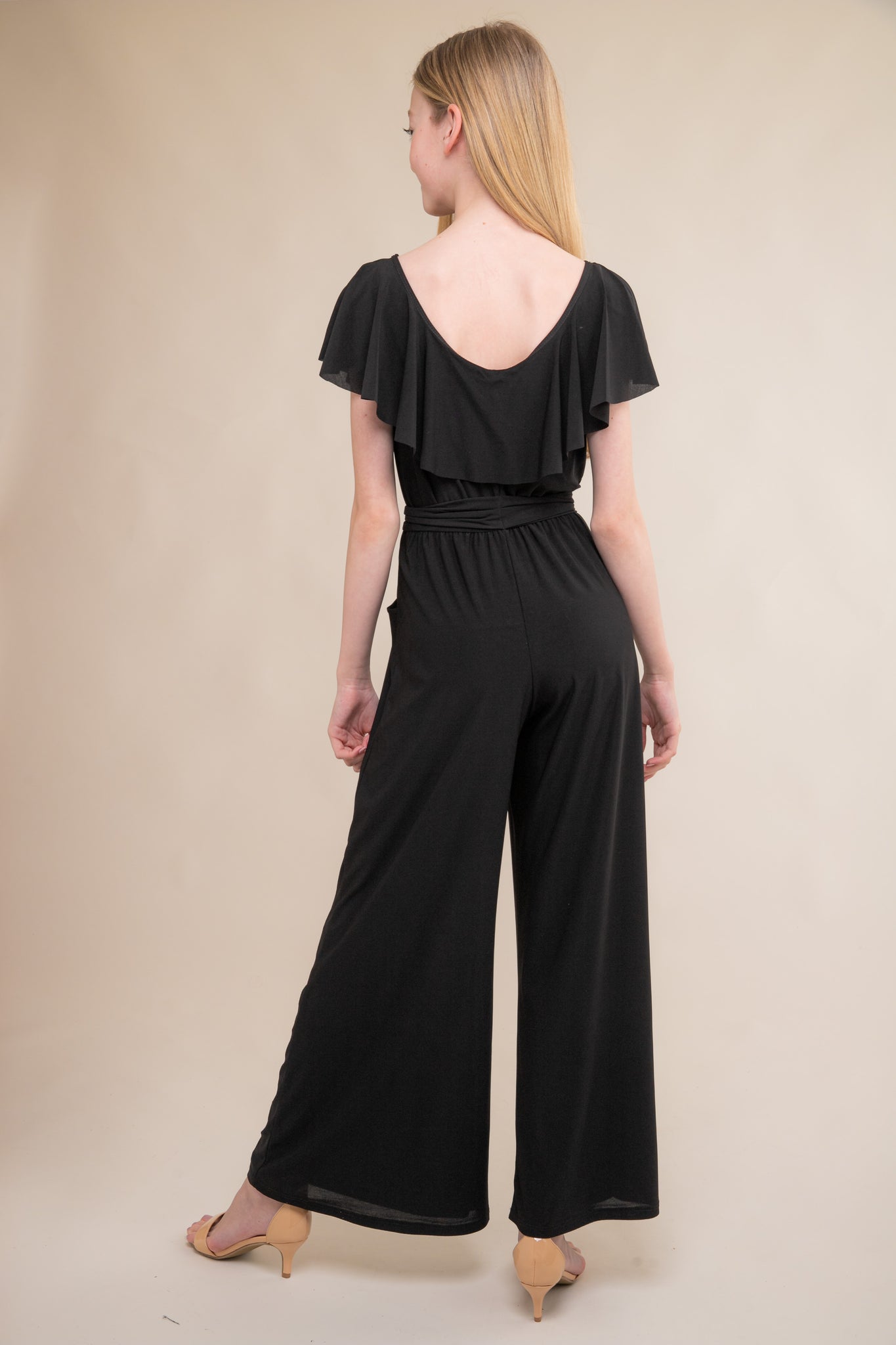 This is the back of the all over stretch jumpsuit in black with flutter off the shoulder sleeve and knotted belt. Features two real pockets and wide leg detailing.