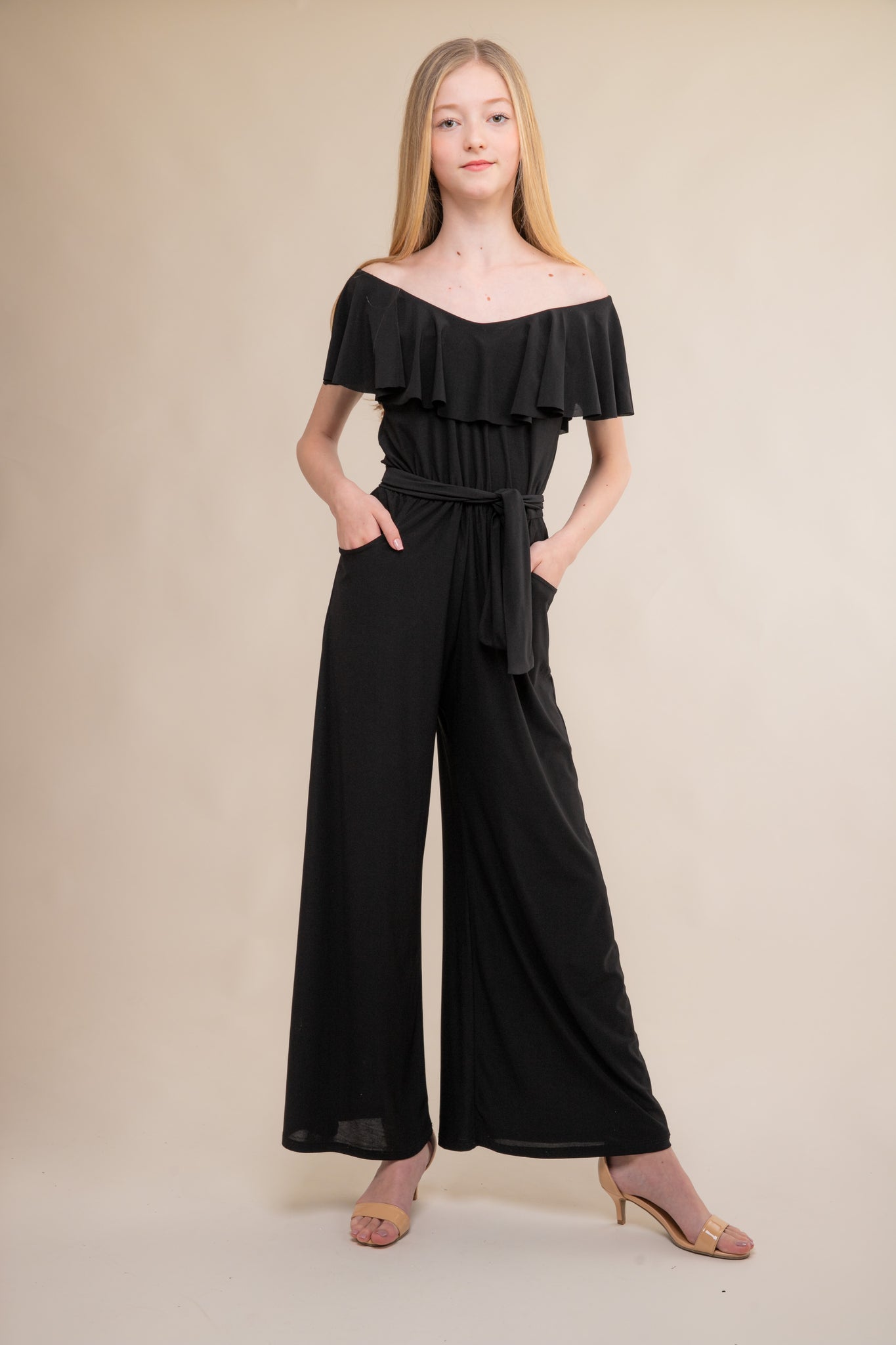 This is the all over stretch jumpsuit in black with flutter off the shoulder sleeve and knotted belt. Features two real pockets and wide leg detailing.