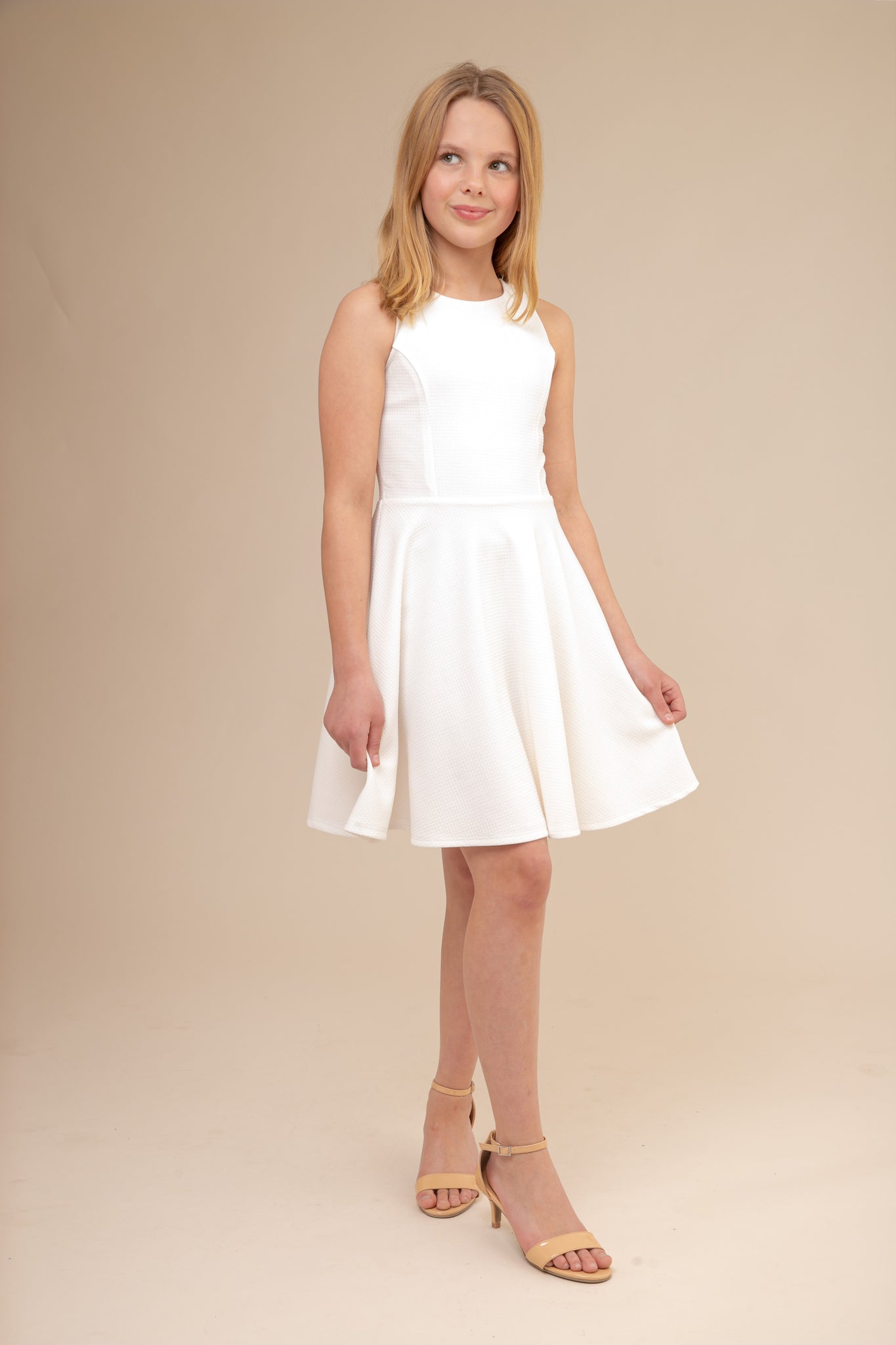 The tank style sleeve textured fit and flare dress is shown in ivory with high neck line, racerback detailing and dart bodice for a chic and sophisticated look. This dress can be worn to a more conservative special occasion event like cotillion, graduation, or religious service like a bat mitzvah service or church ceremony.