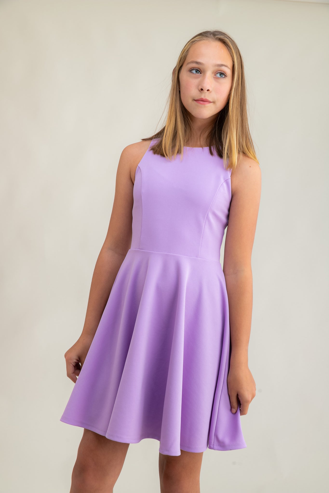 The tank style sleeve textured fit and flare dress is shown in lilac with high neck line, racerback detailing and dart bodice for a chic and sophisticated look. This dress can be worn to a more conservative special occasion event like cotillion, graduation, or religious service like a bat mitzvah service or church ceremony.