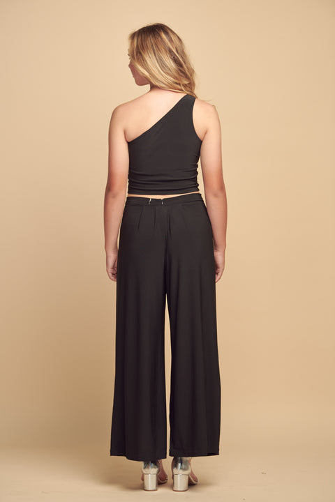 Blonde girl in a black one shoulder crop top and wide leg black pant.
