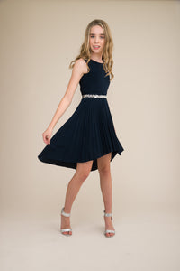 Blonde girl in a fit and flare dress with pleated high low skirt and belt.
