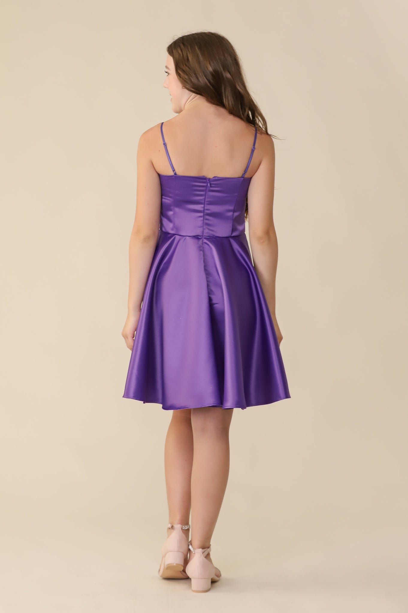 Brown haired girl wearing rich, purple satin party dress hitting above the knee with a sparkle heel shoe.