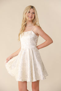 A young blonde haired girl in the fit and flare silver and ivory dress that hits above the knee.