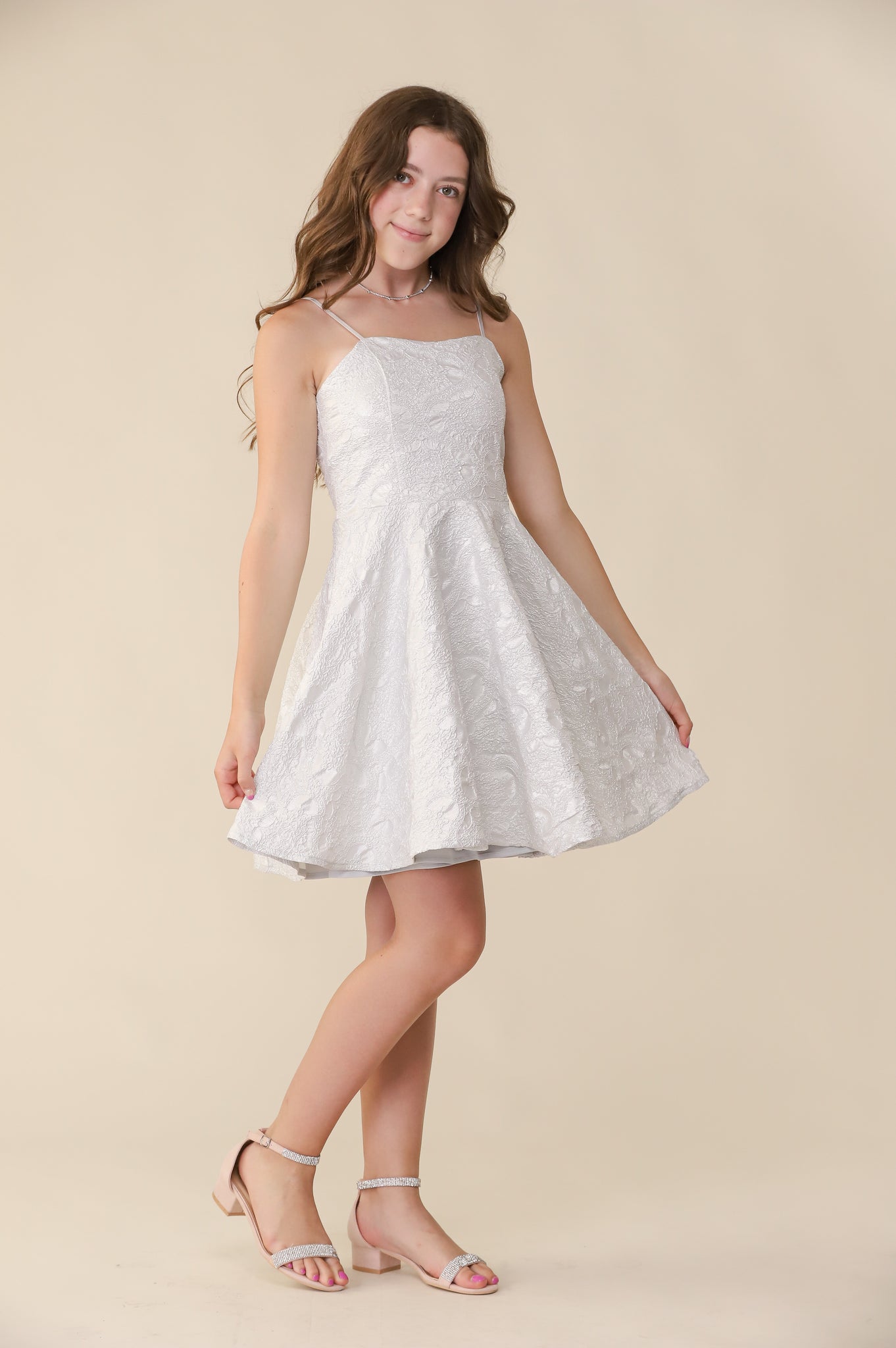 A young brown haired girl in the fit and flare silver and ivory dress that hits above the knee with a heel..